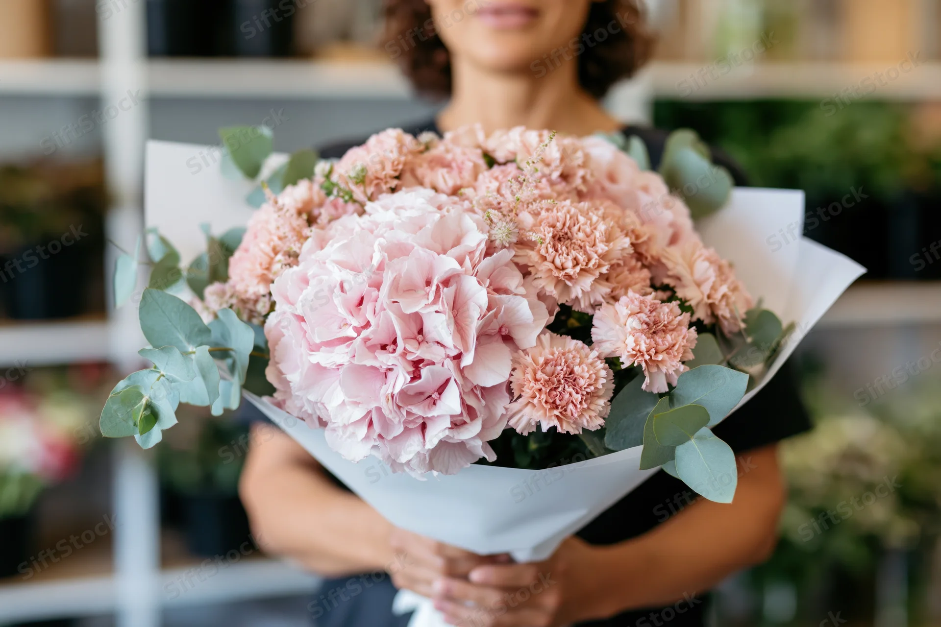 Woman holding a large bouquet of blush pink hyacinths and carnations with eucalyptus in a flower shop
