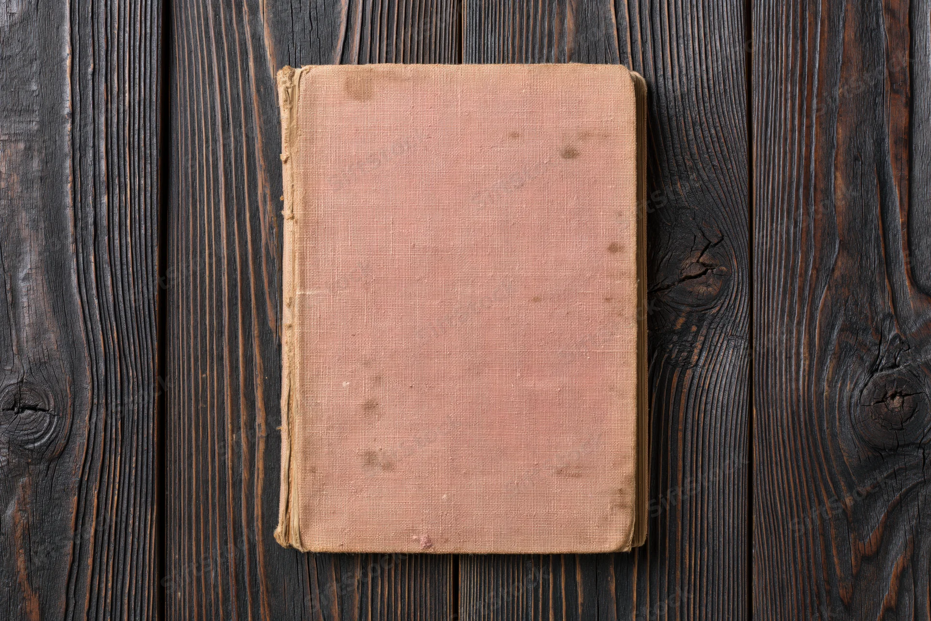Worn antique book with blank faded cover lying flat on dark wooden surface