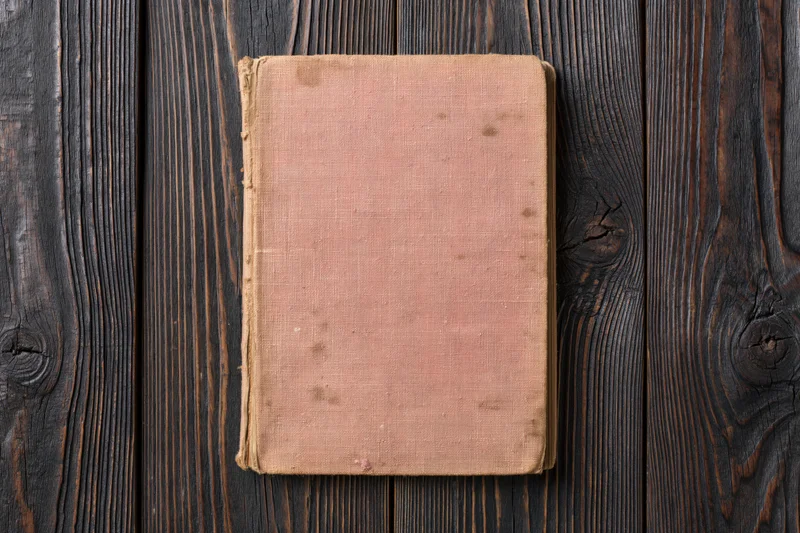 Worn antique book with blank faded cover lying flat on dark wooden surface