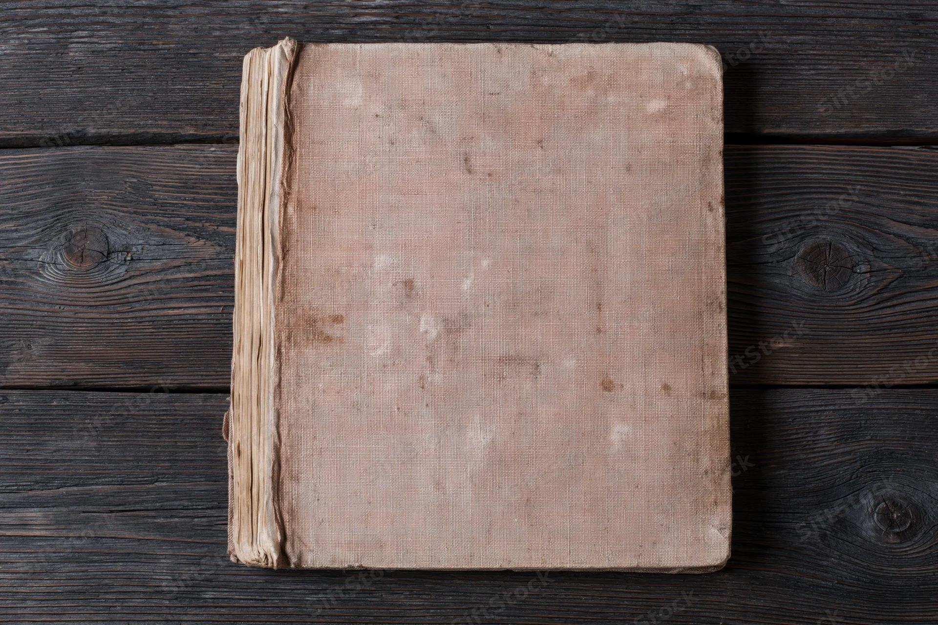 Worn antique book with blank faded cover lying flat on dark wooden surface