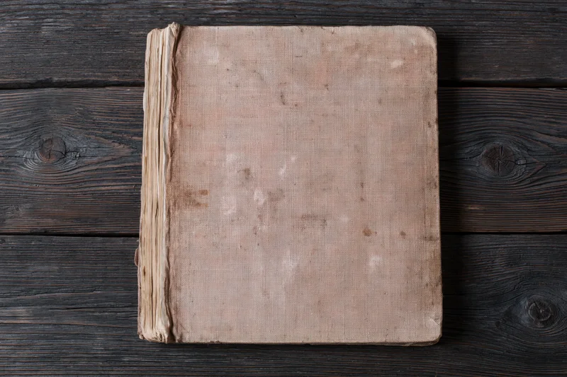 Worn antique book with blank faded cover lying flat on dark wooden surface
