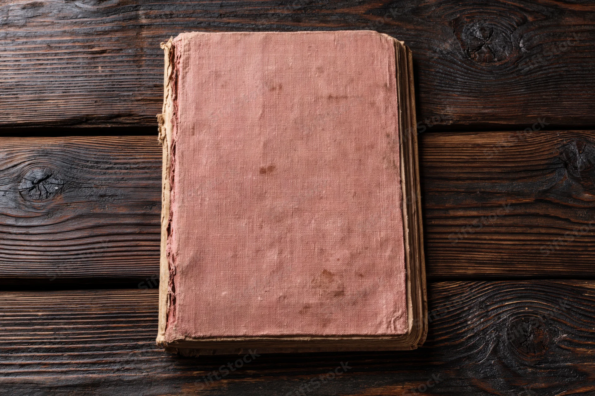 Worn antique book with blank faded pink cover lying flat on dark wooden surface