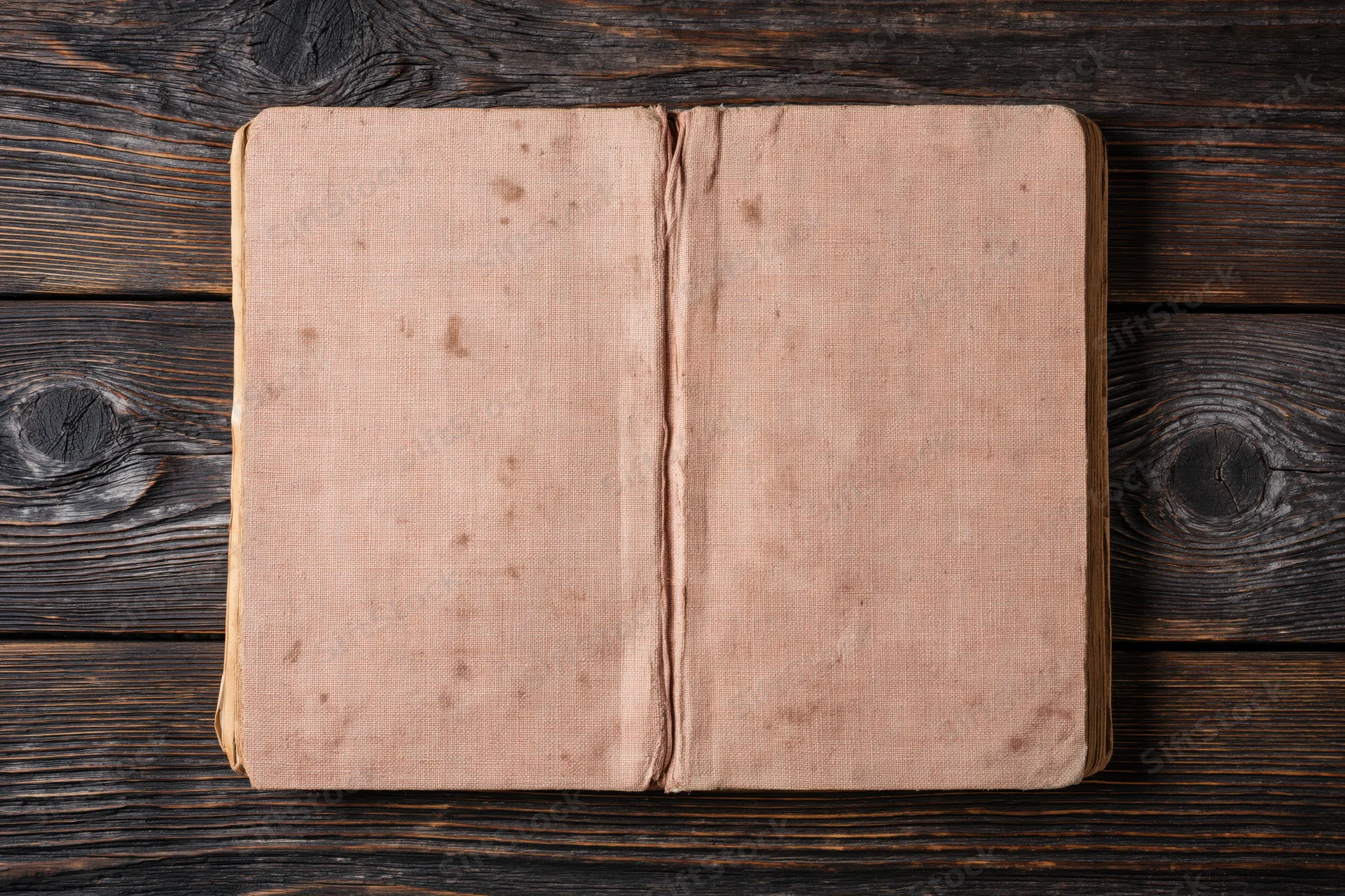 Worn antique book lying flat open on dark wooden surface with blank faded cover facing up