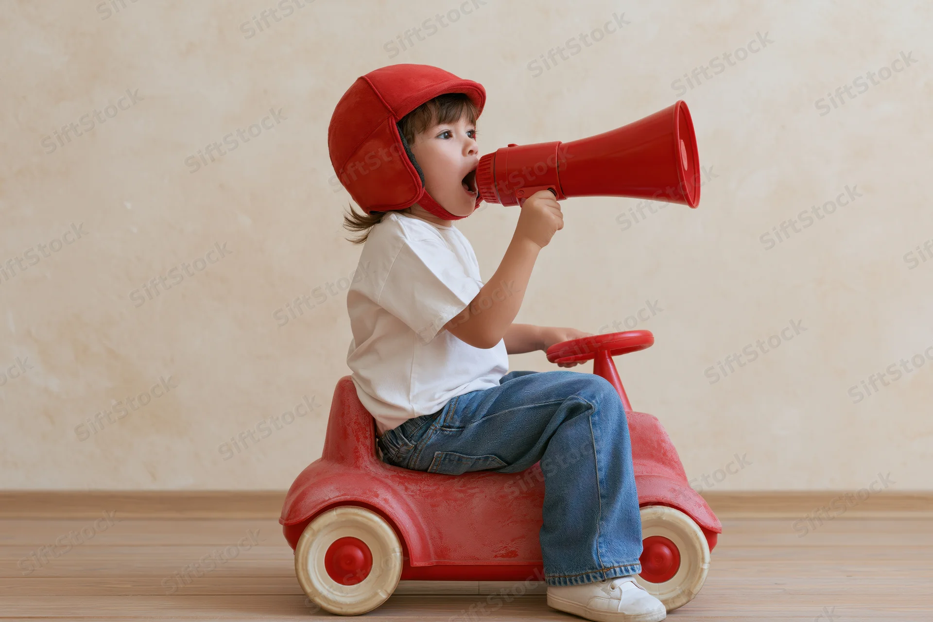 Young child in red pedal car holding megaphone indoors