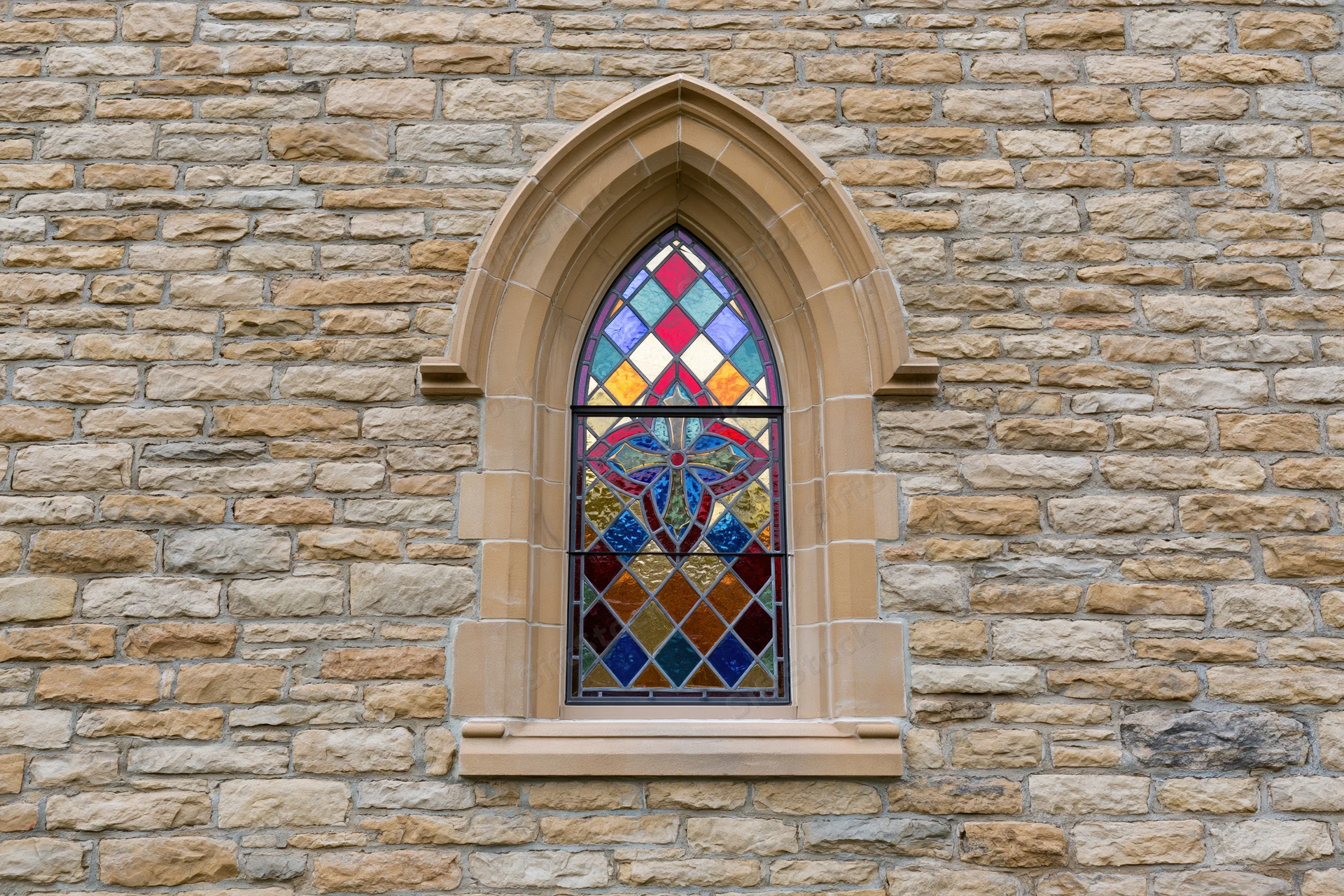 Gothic arched stained glass window set into rough limestone wall of church exterior