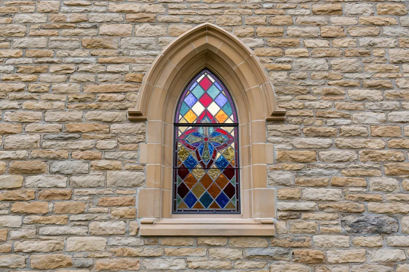 Gothic arched stained glass window set into rough limestone wall of church exterior