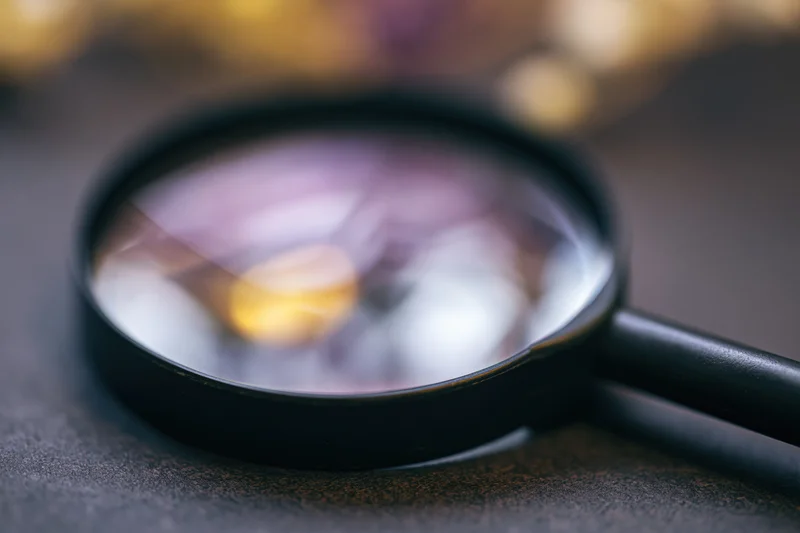 Black magnifying glass resting on dark textured surface with blurred background