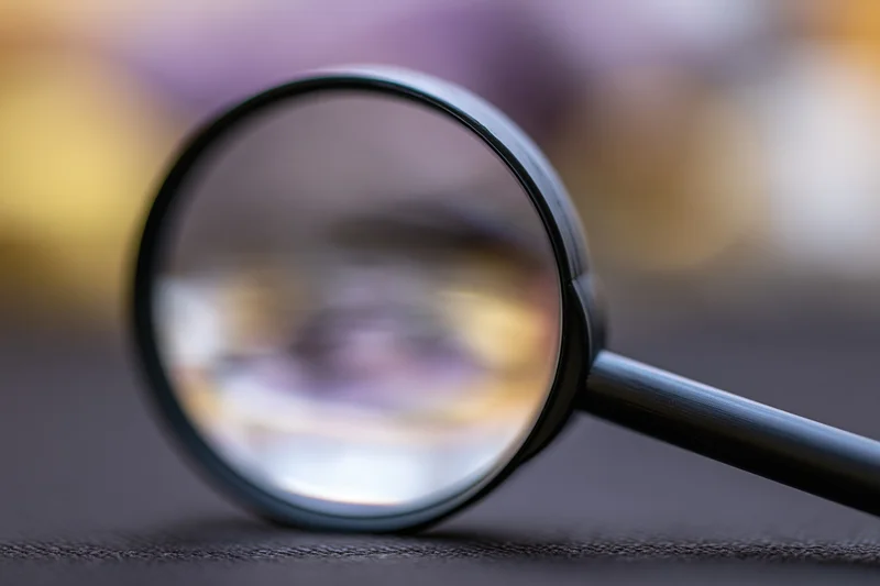 Black magnifying glass resting on dark textured surface with blurred background