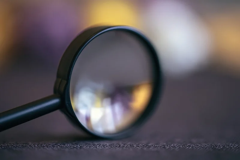 Black magnifying glass resting on dark textured surface with blurred background and reflection in lens