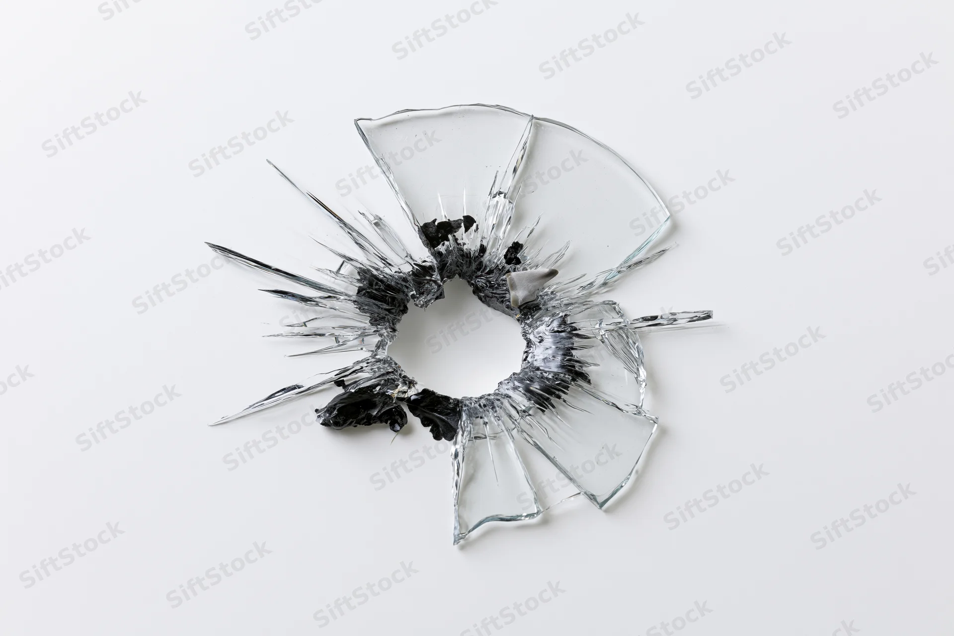 Shattered glass pane with central bullet hole and radial cracks on white background