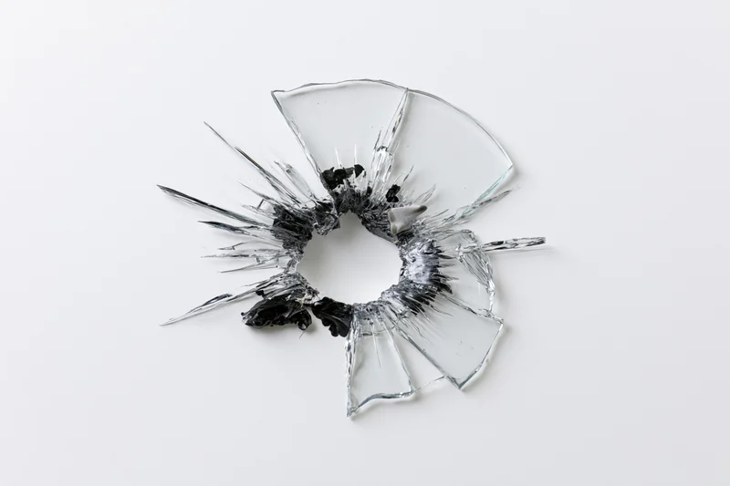 Shattered glass pane with central bullet hole and radial cracks on white background