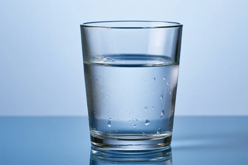 Clear glass tumbler filled with water sitting on a reflective blue surface