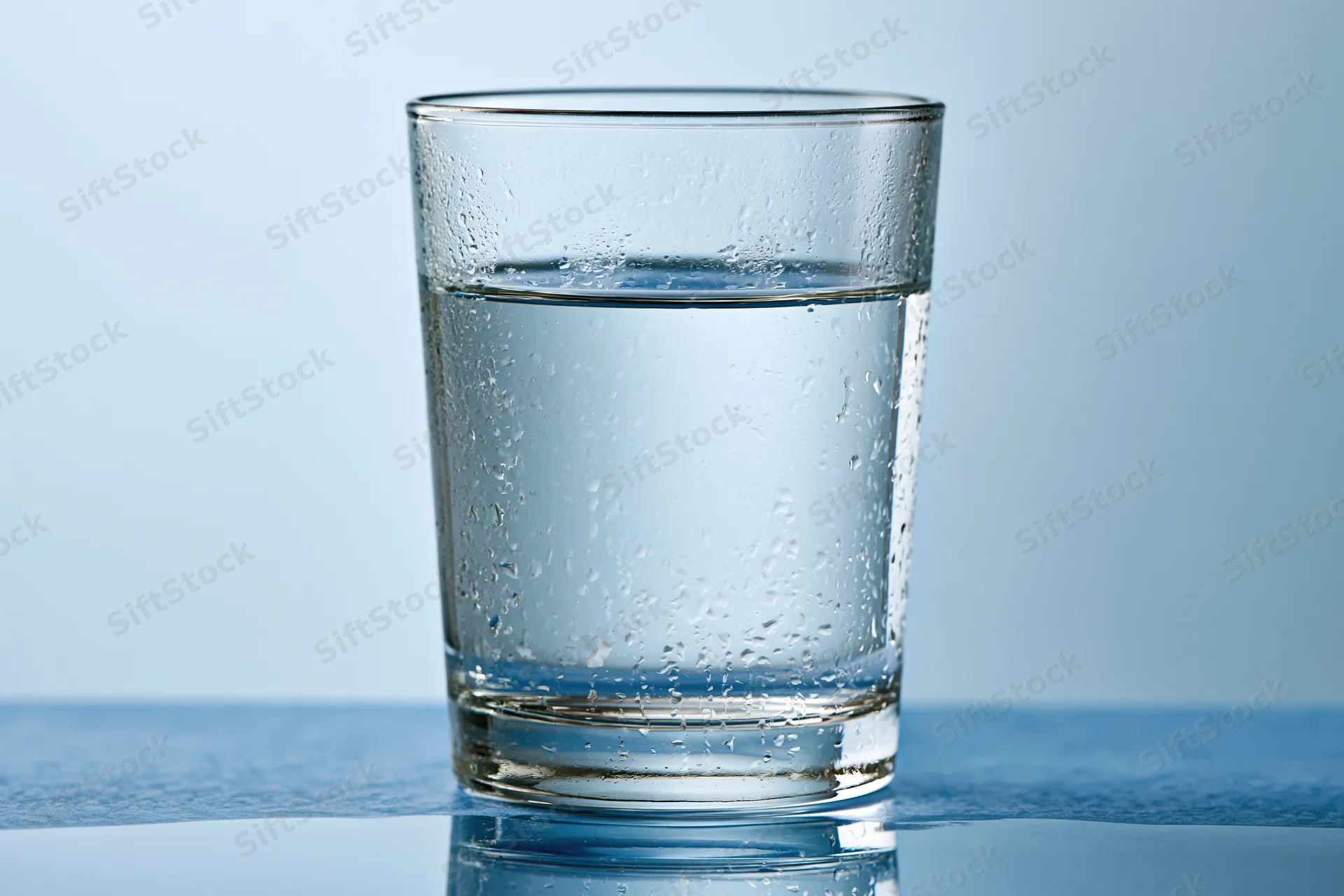 Clear glass tumbler filled with water sitting on a reflective blue surface
