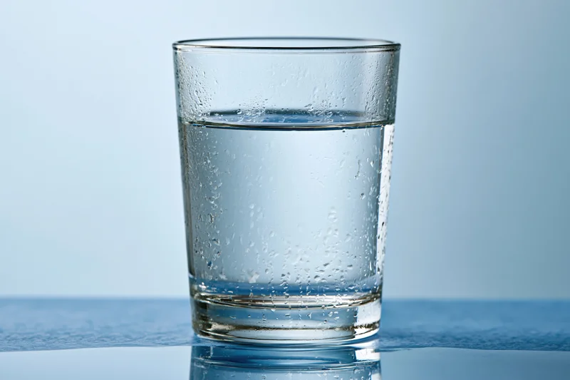 Clear glass tumbler filled with water sitting on a reflective blue surface