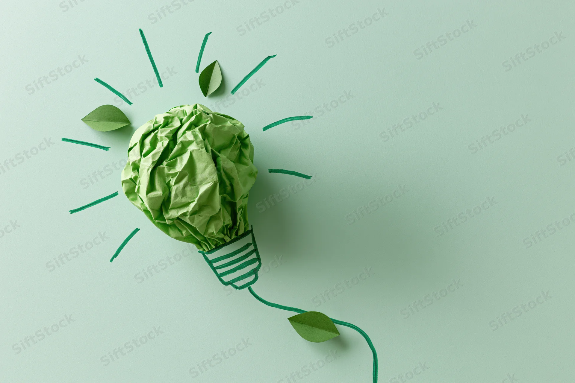 Crumpled green paper shaped as a lightbulb with drawn rays and leaves on a flat surface