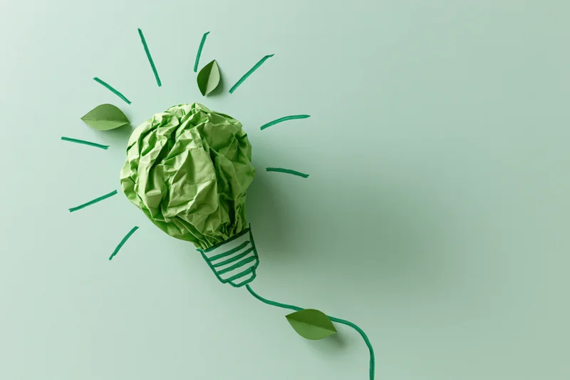 Crumpled green paper shaped as a lightbulb with drawn rays and leaves on a flat surface