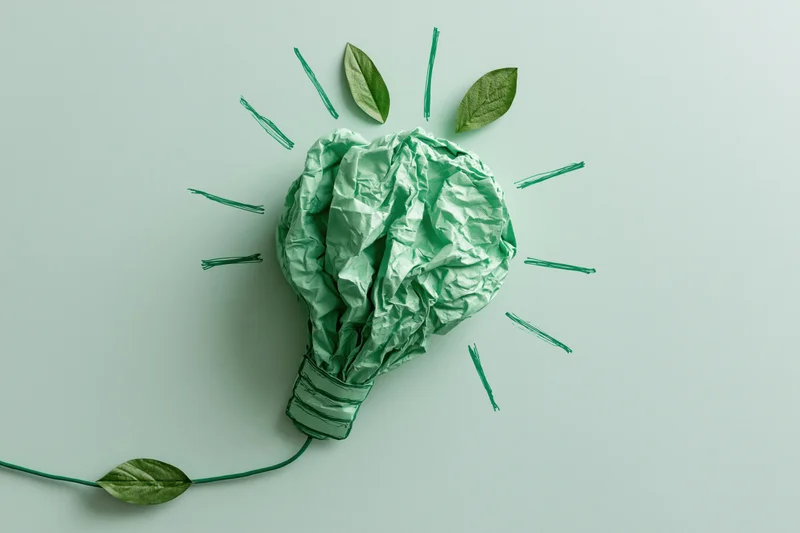 Crumpled green paper shaped as a lightbulb with leaves and drawn rays on a flat surface