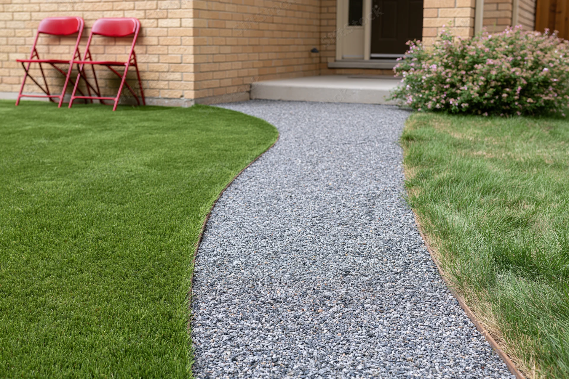 Curved gravel pathway winding through a front yard with green lawn and brick house entrance