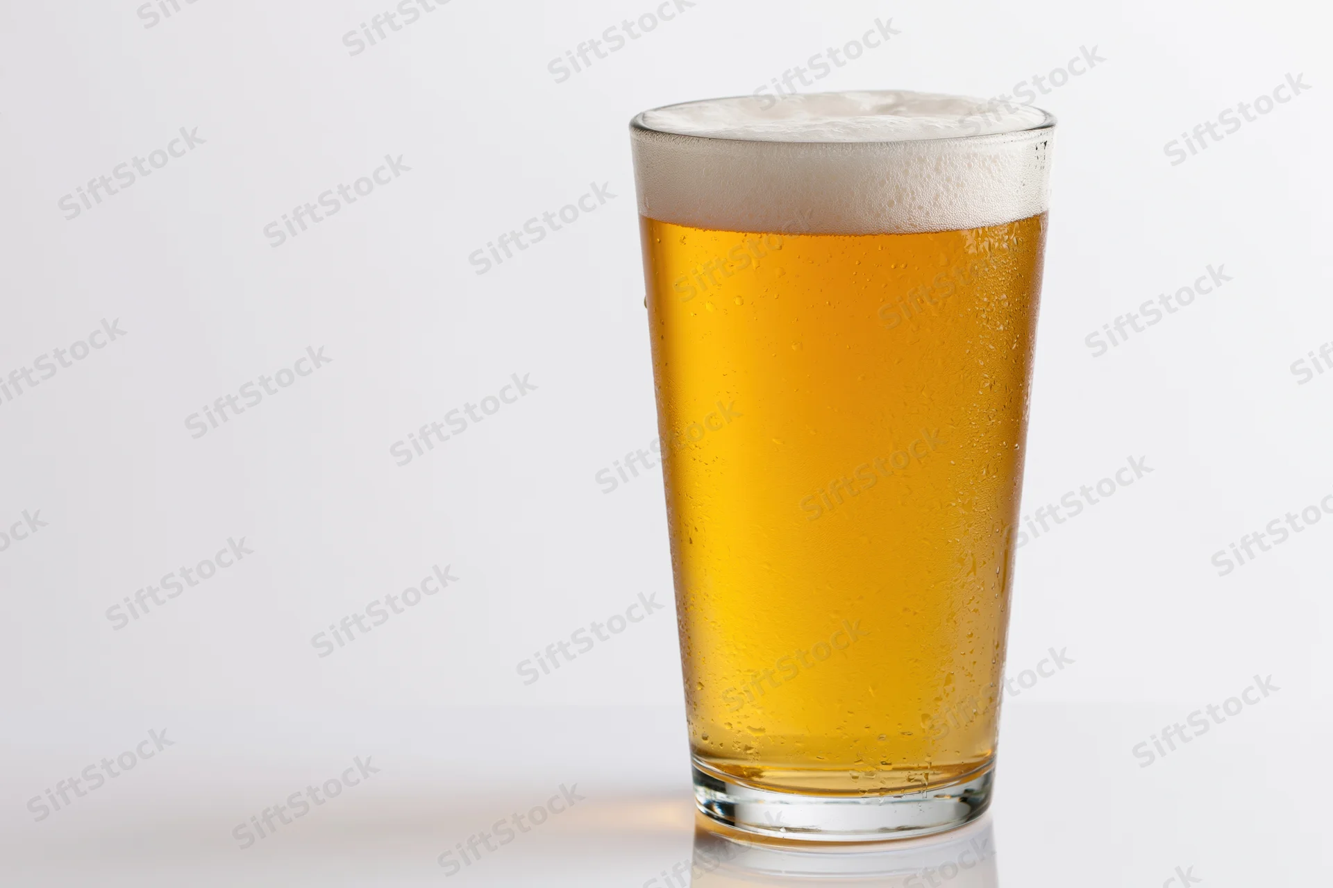 Full pint glass of pale lager with white foam head on white background
