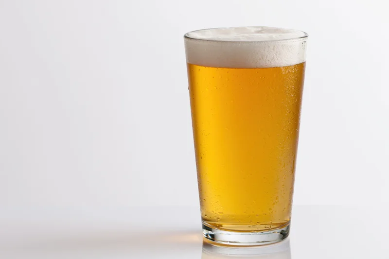 Full pint glass of pale lager with white foam head on white background