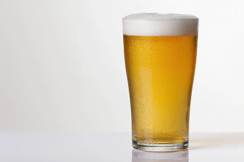 Full pint glass of pale lager with white foam head on white background