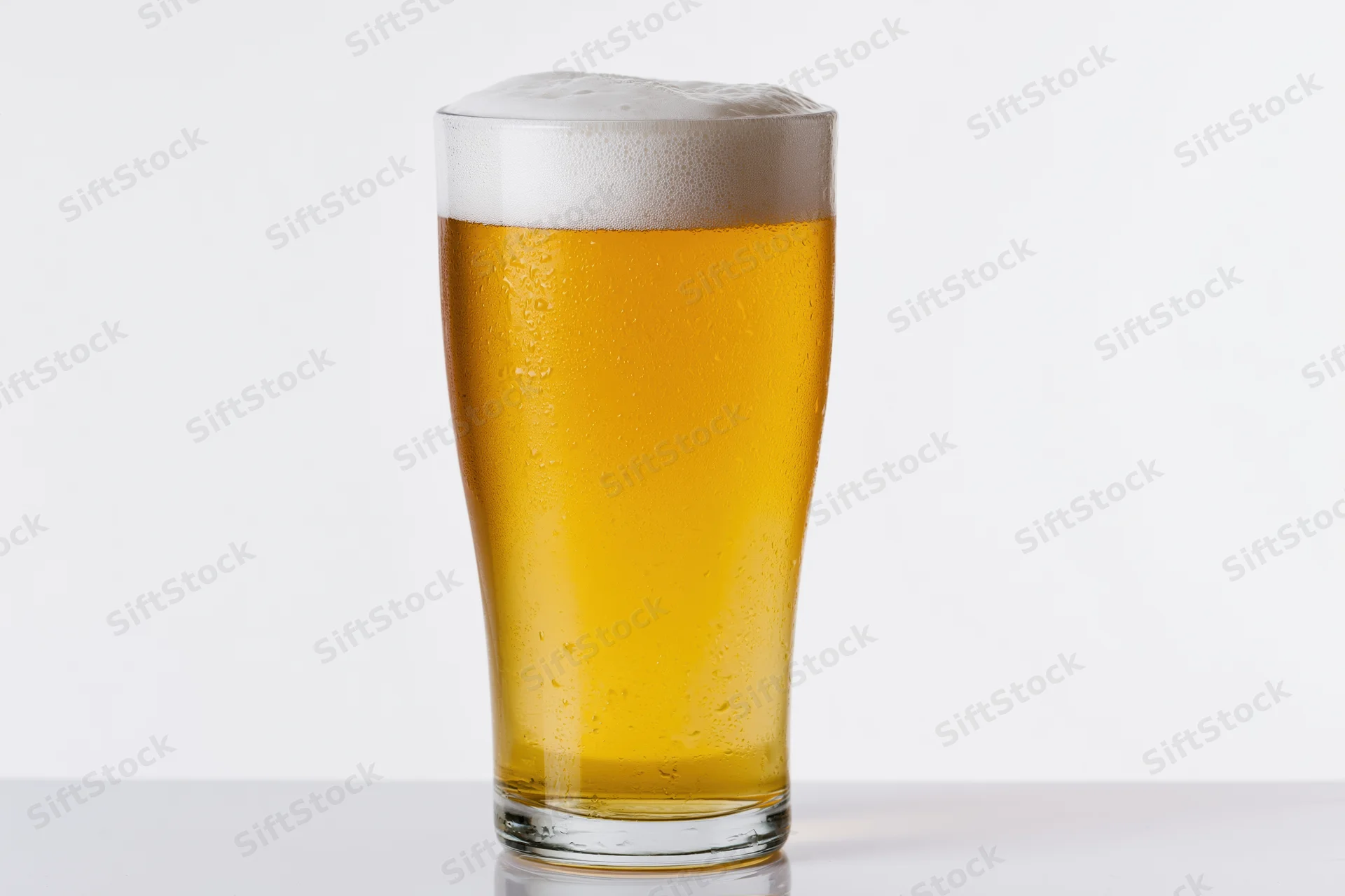 Full pint glass of pale lager with white foam head on white surface