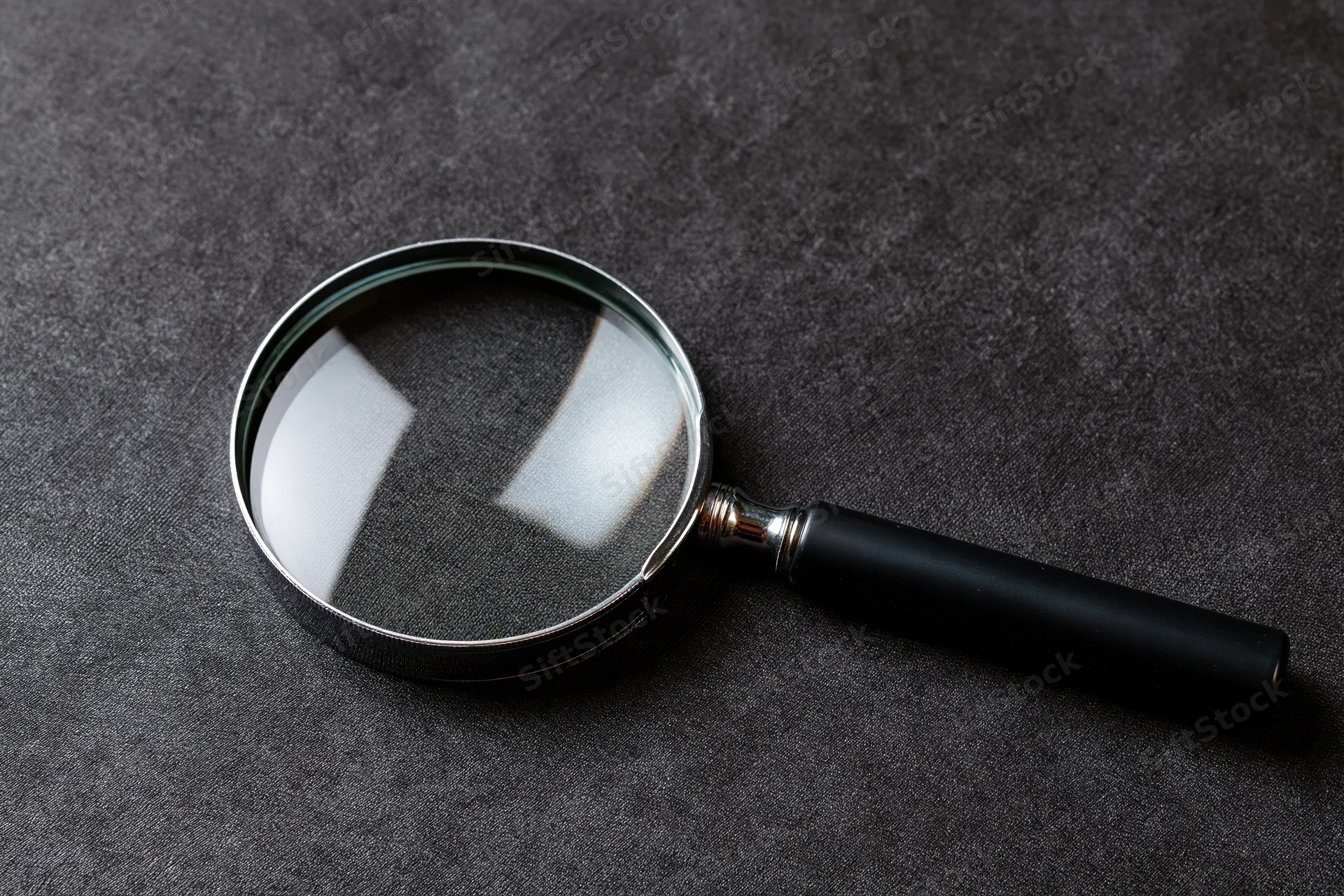 Magnifying glass with black handle resting at an angle on dark textured surface