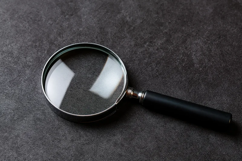 Magnifying glass with black handle resting at an angle on dark textured surface
