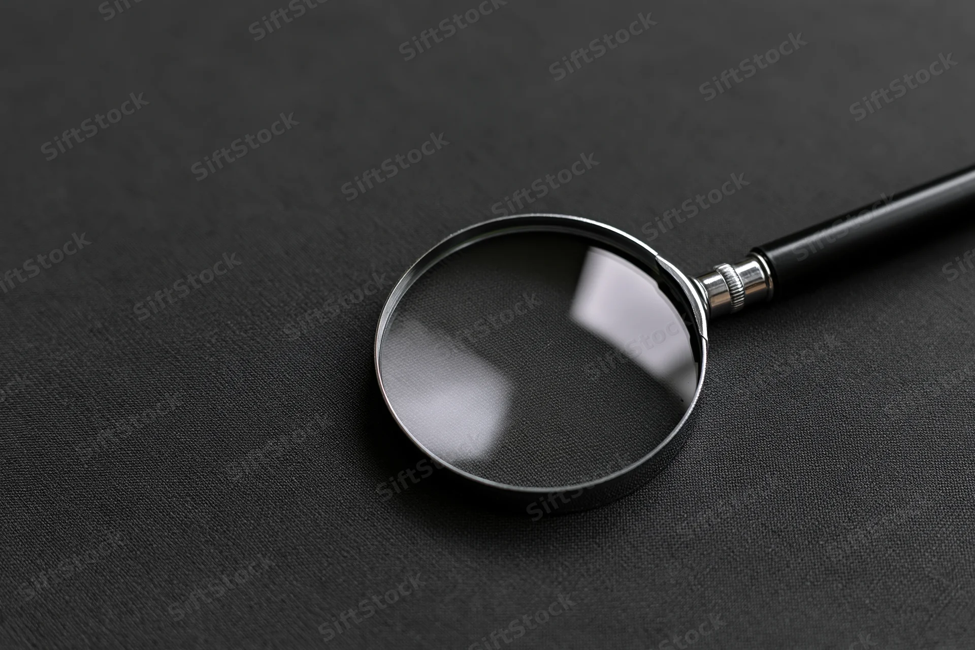 Magnifying glass with black handle resting at an angle on dark textured surface