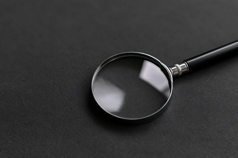 Magnifying glass with black handle resting at an angle on dark textured surface