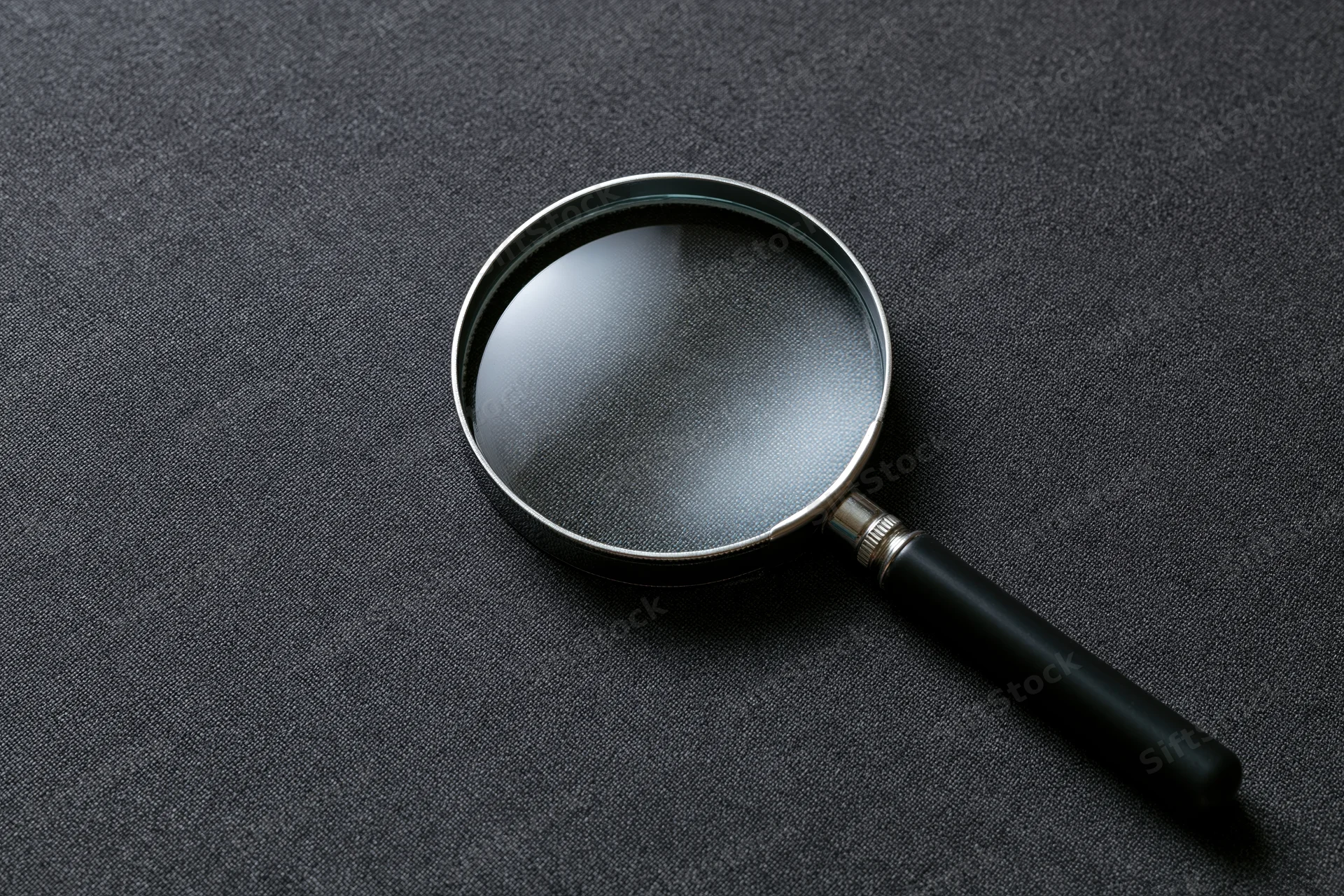 Magnifying glass with black handle resting at an angle on dark textured surface
