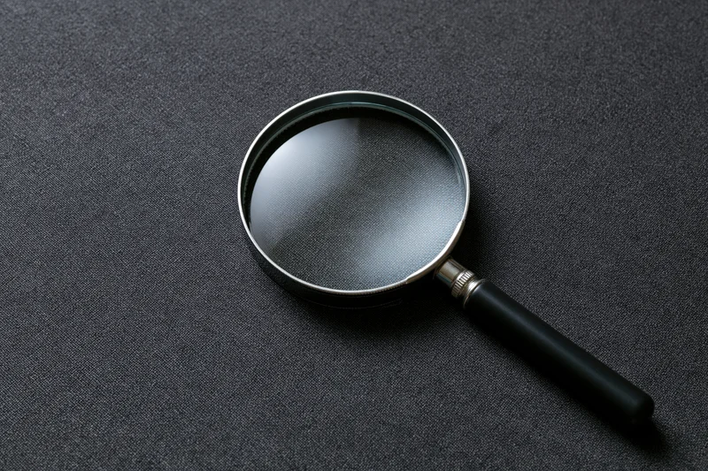 Magnifying glass with black handle resting at an angle on dark textured surface