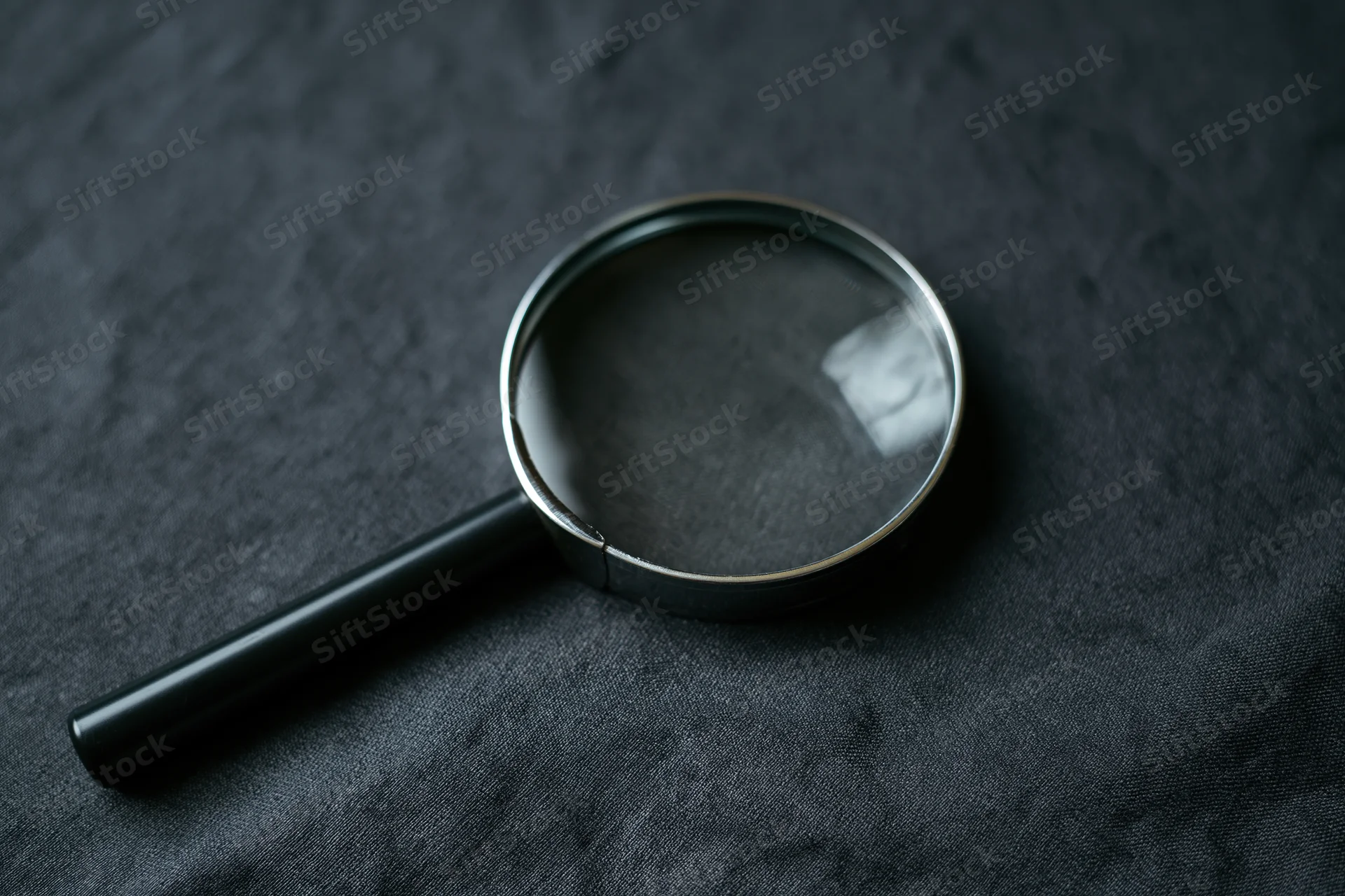 Magnifying glass with black handle resting at an angle on dark textured fabric
