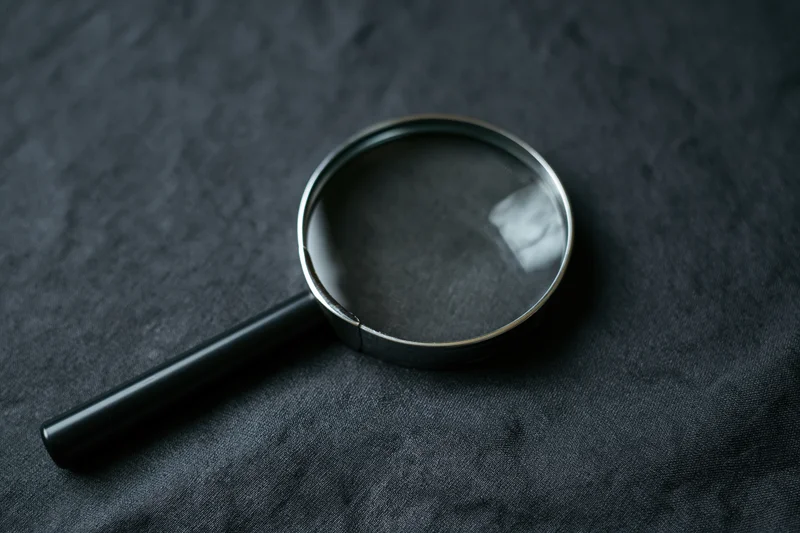 Magnifying glass with black handle resting at an angle on dark textured fabric