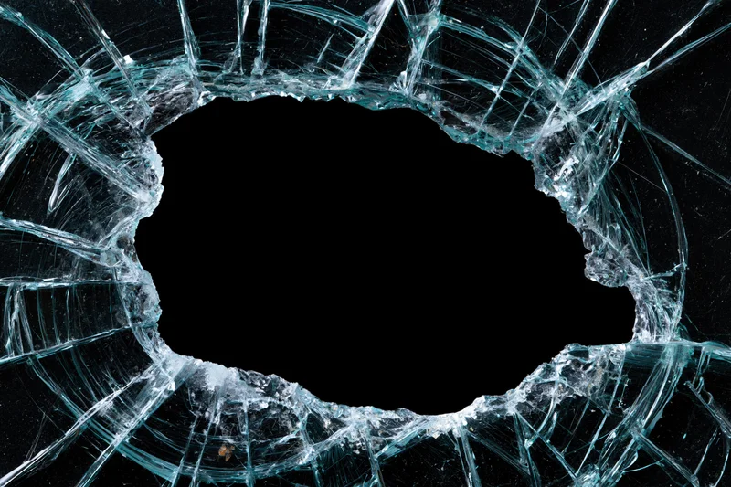 Shattered glass pane with large oval hole and radiating cracks against black background