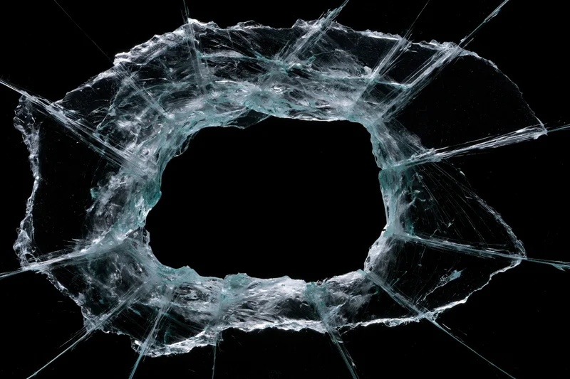 Shattered glass pane with large rectangular hole and radiating cracks against black background