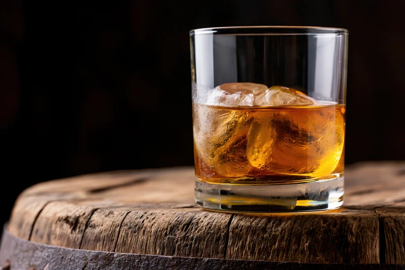 Amber whiskey in a rocks glass with ice on a wooden barrel top