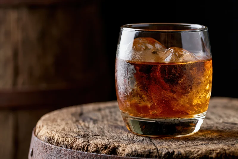 Amber whiskey in a rocks glass with ice on a wooden barrel top