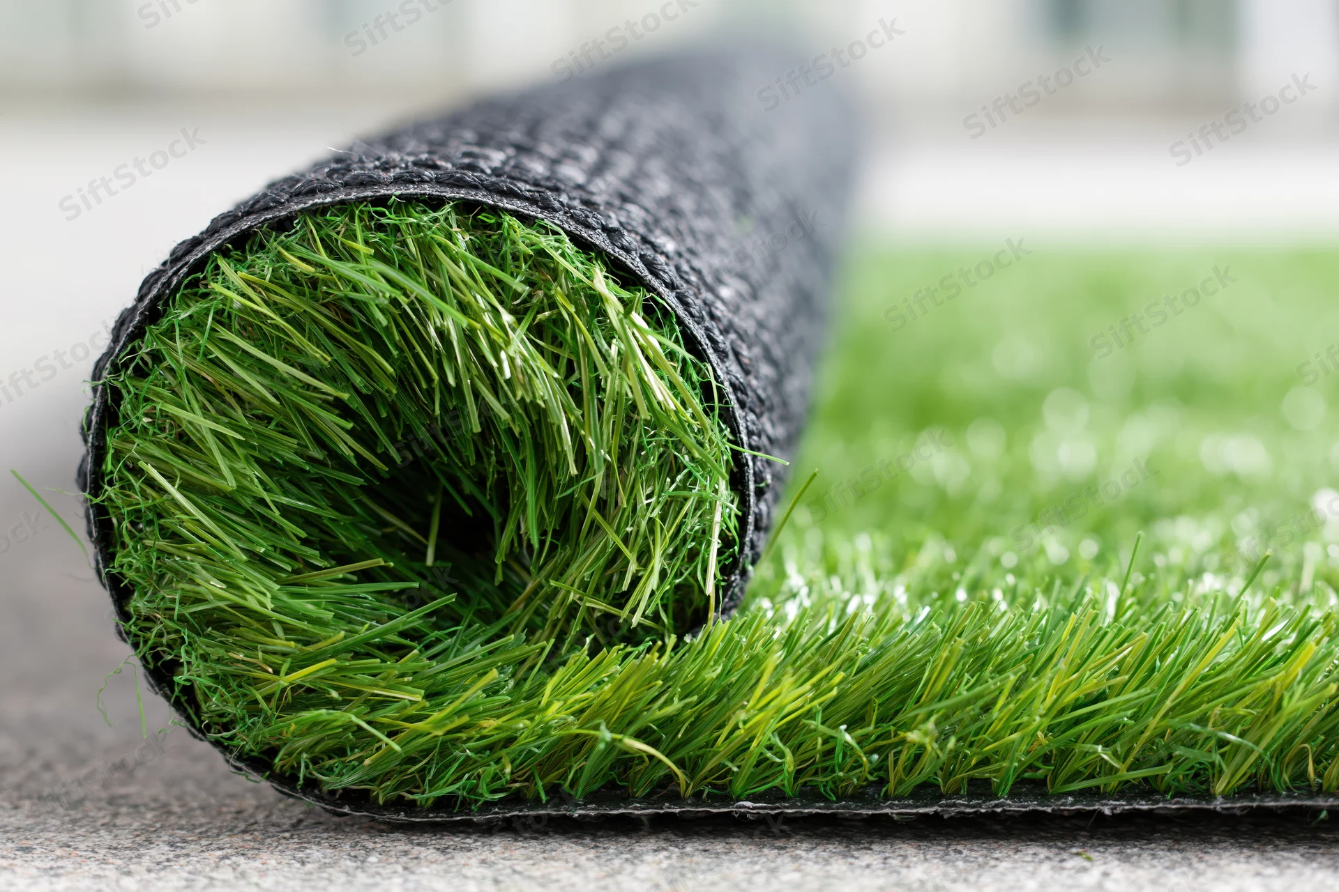 Roll of artificial grass turf partially unrolled on a concrete surface