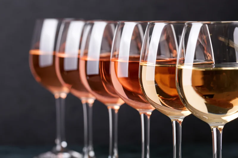Row of stemmed wine glasses filled with varying shades of rosé and white wine arranged in a line on a dark surface