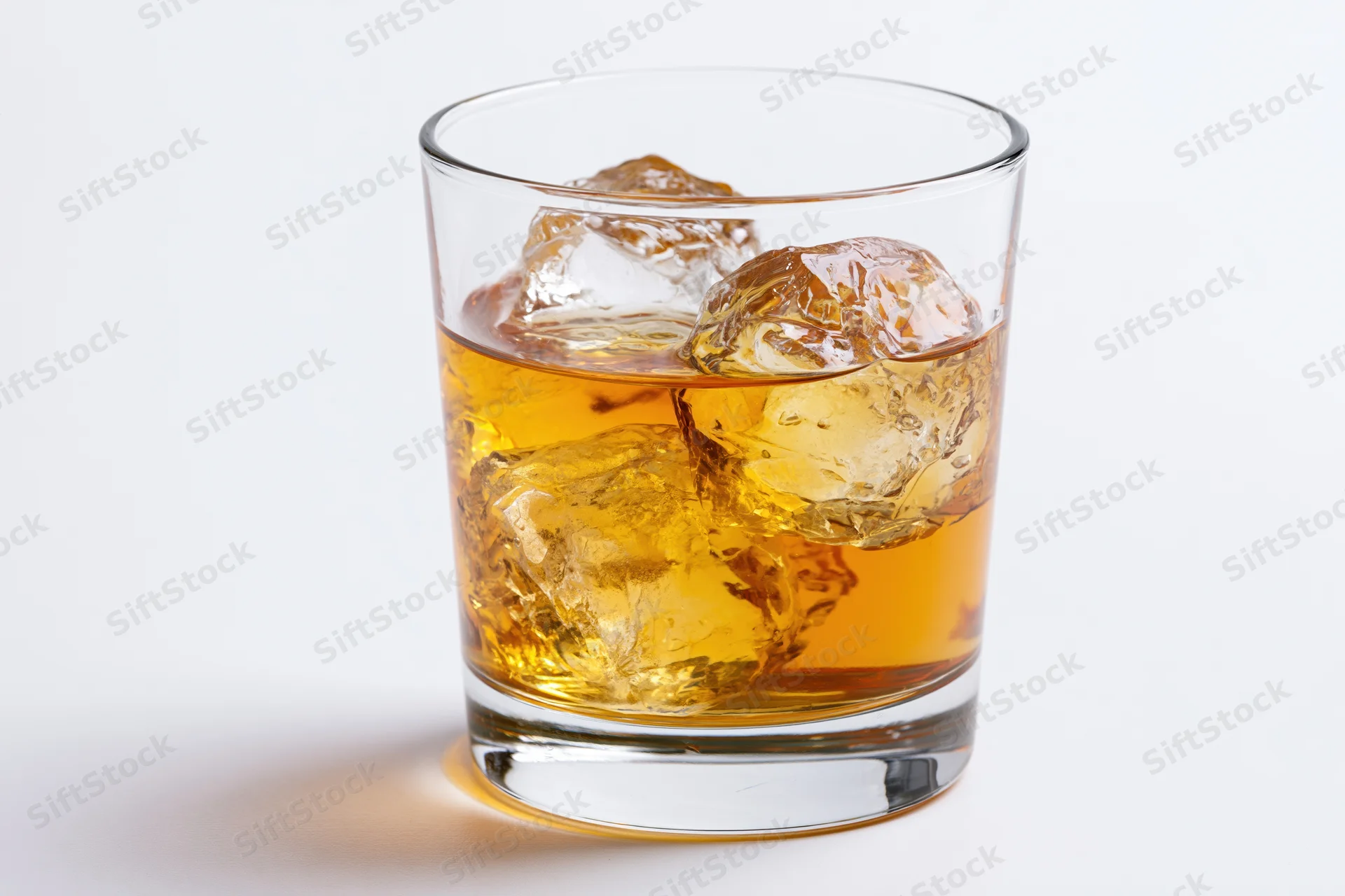 Short rocks glass filled with amber whiskey and ice cubes on white background