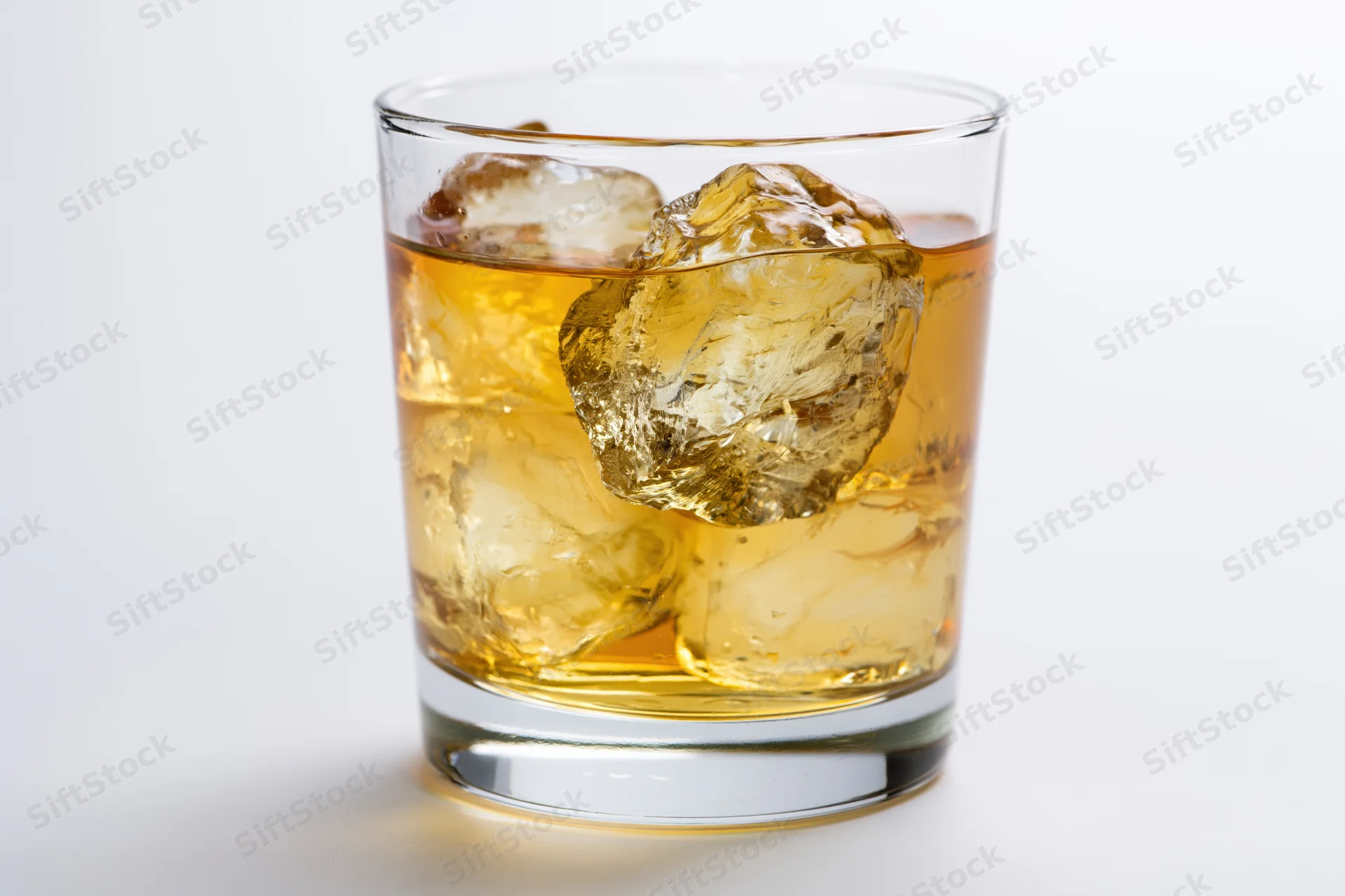 Short rocks glass filled with amber whiskey and ice cubes on white background