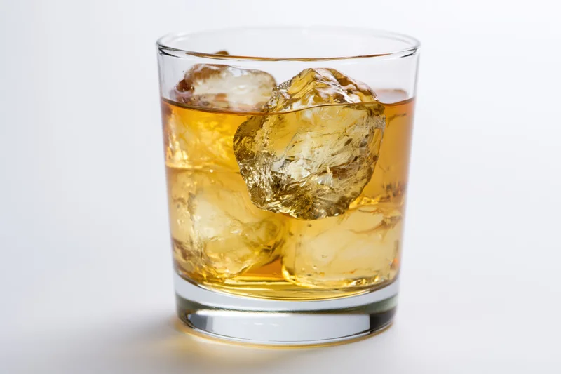 Short rocks glass filled with amber whiskey and ice cubes on white background