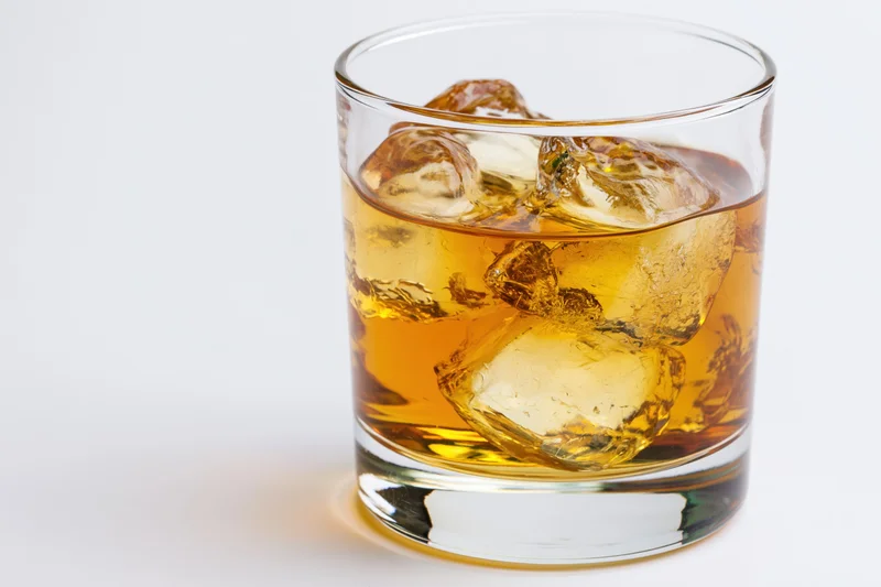 Short rocks glass filled with amber whiskey and ice cubes on white background