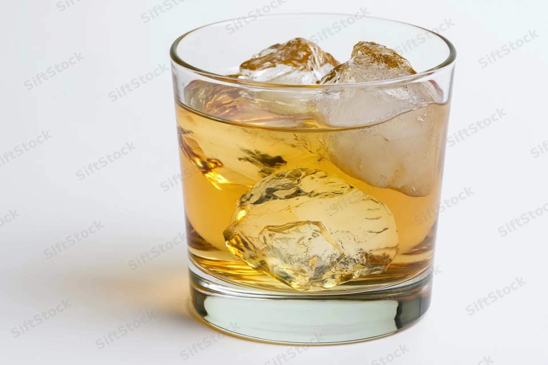 Short rocks glass filled with amber whiskey and large ice cubes on white background