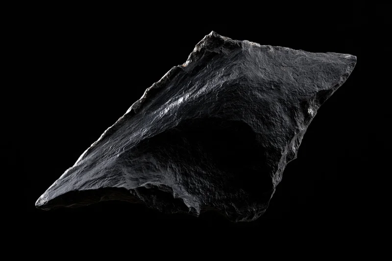 Rough obsidian stone fragment floating against black background