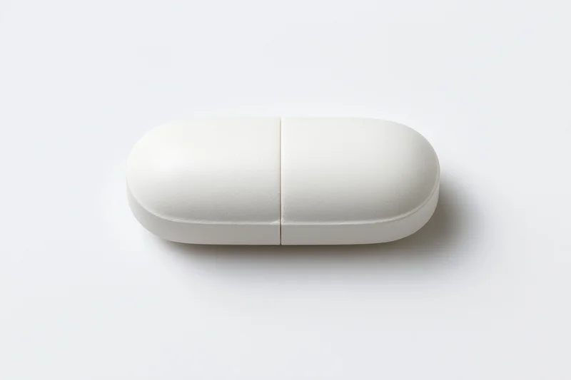 White oval pill capsule lying flat centered on plain white surface