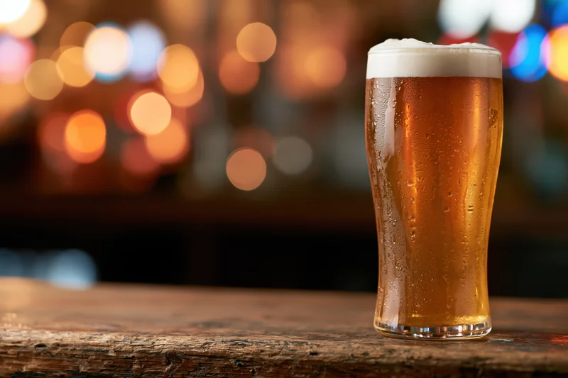 Cold lager in a tall glass with foamy head on a wooden bar counter