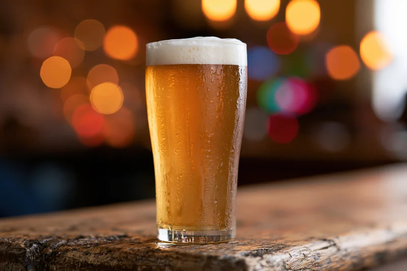 Cold lager in a tall glass with foamy head on a wooden bar surface