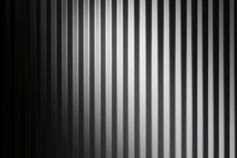 Close-up of a corrugated metal surface with vertical ribs and a gradient of gray tones